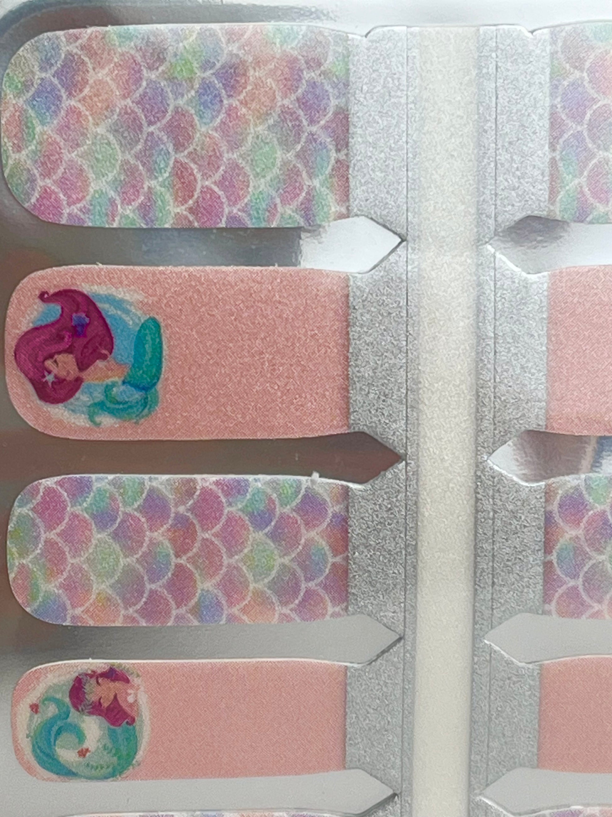 Mermaid-themed nail polish strips with pastel iridescent scales and pink designs featuring a swimming mermaid.