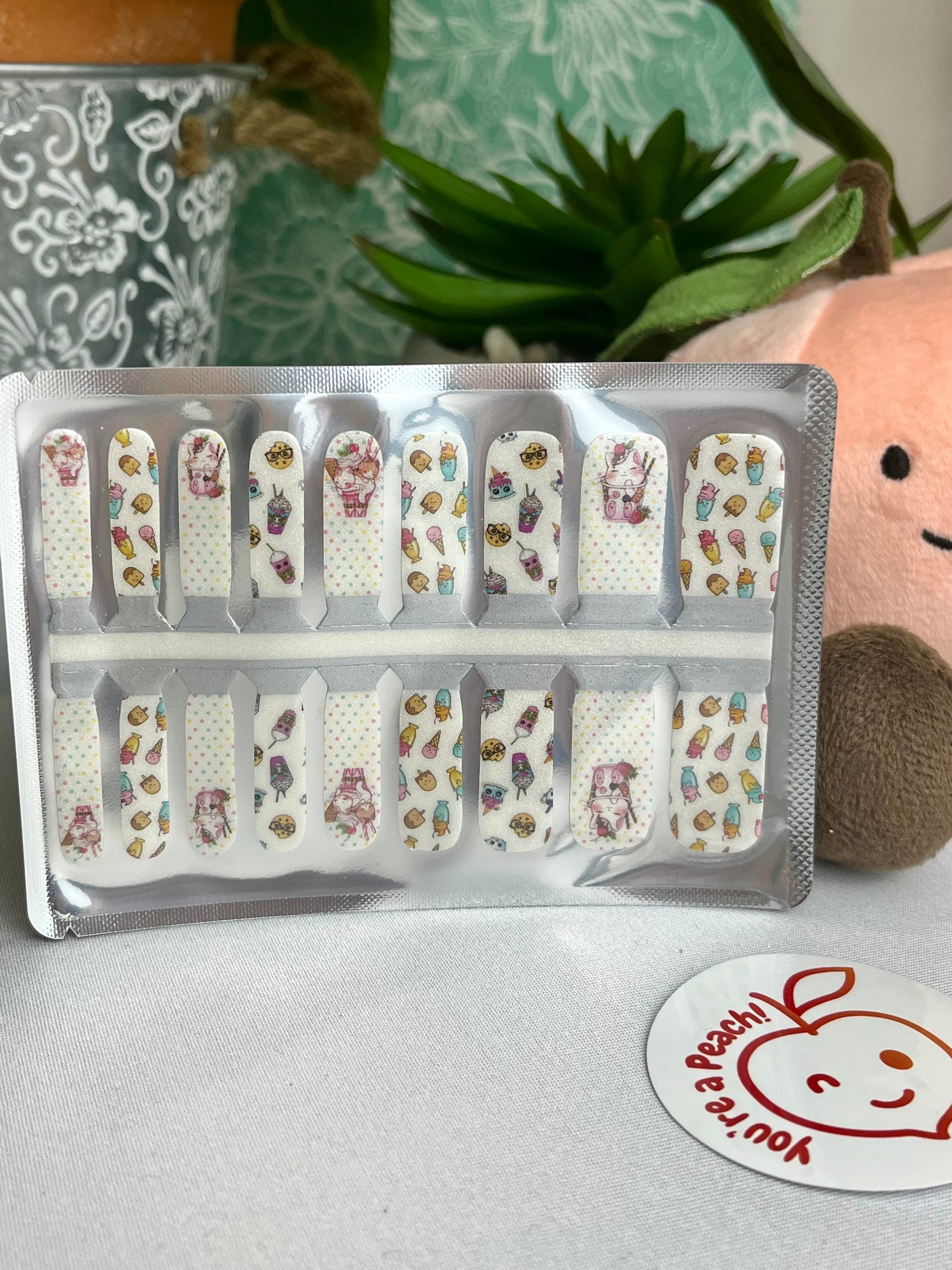 White nail wraps with cute cartoon ice cream, milkshake, and dessert designs on a polka dot background.