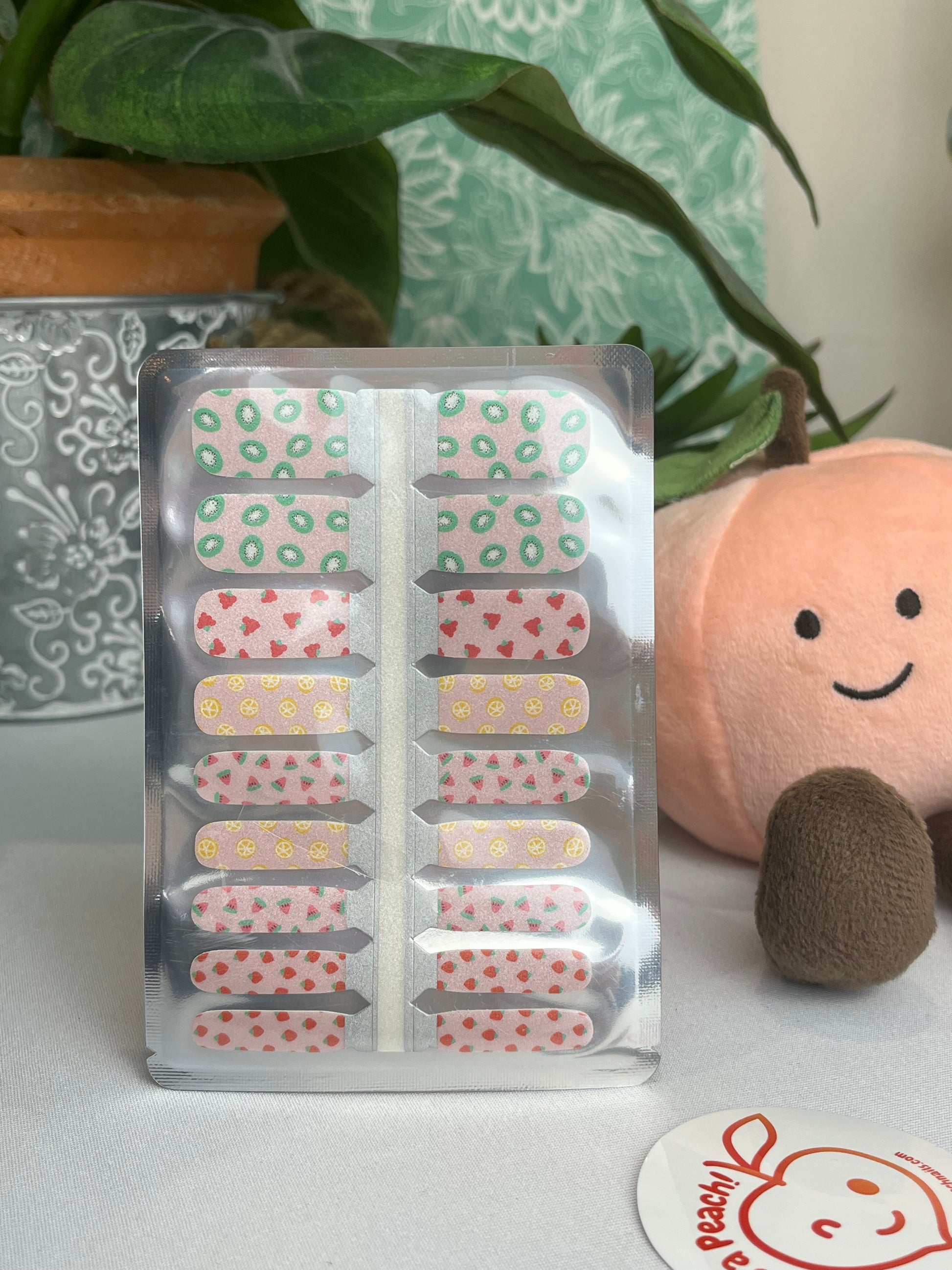 Fruit-patterned nail strips in clear packaging featuring kiwi, strawberry, lemon, and watermelon designs.