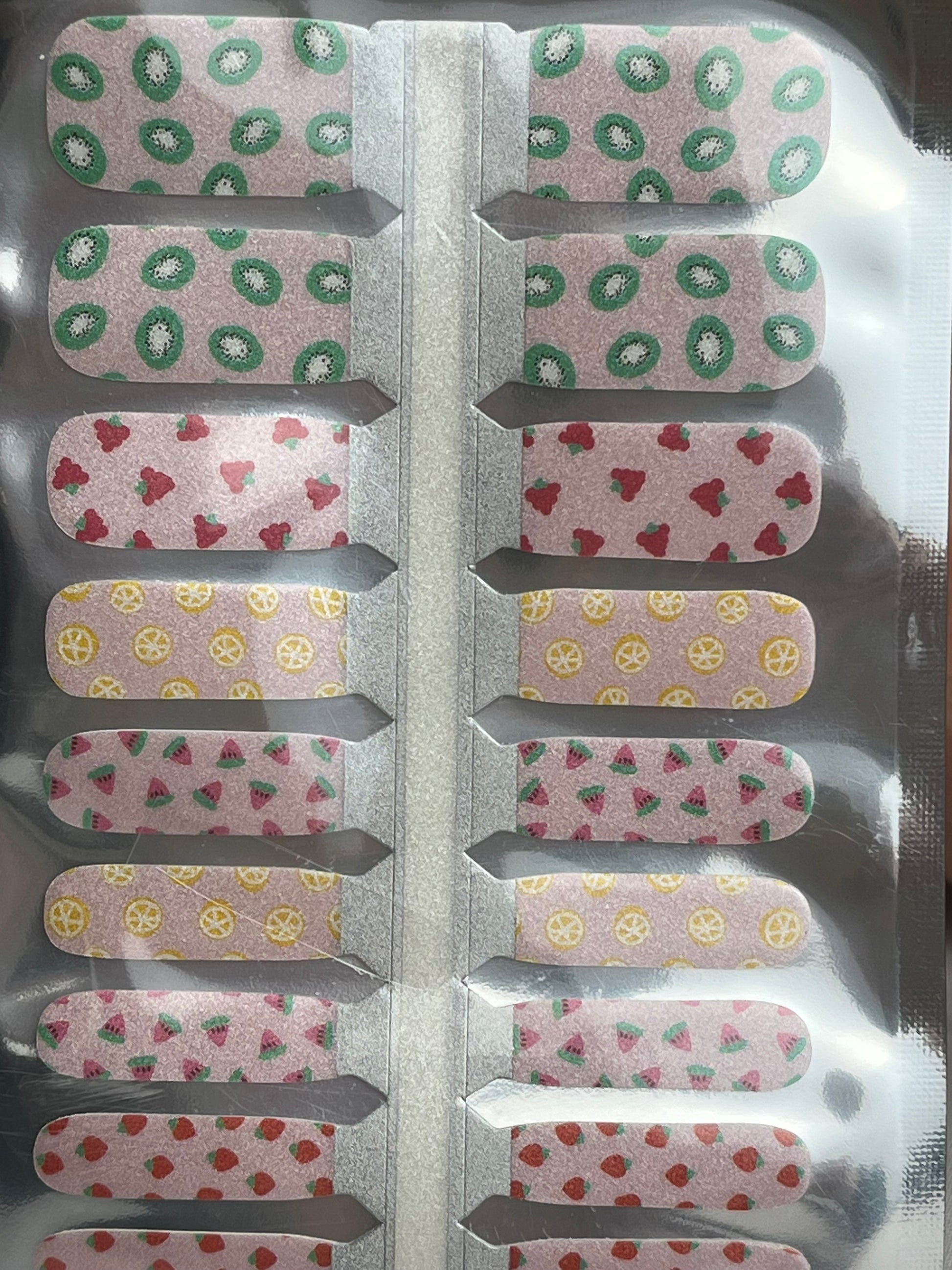 Fruit design nail wraps with kiwi, strawberry, lemon, and watermelon patterns on a light pink background