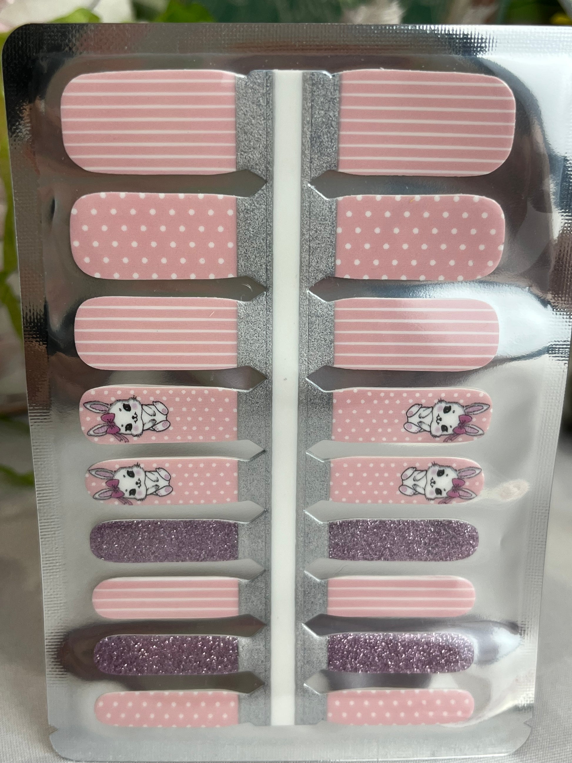 Sheet of pink and purple glitter nail wraps with stripes, polka dots, and cute bunny designs in clear packaging.