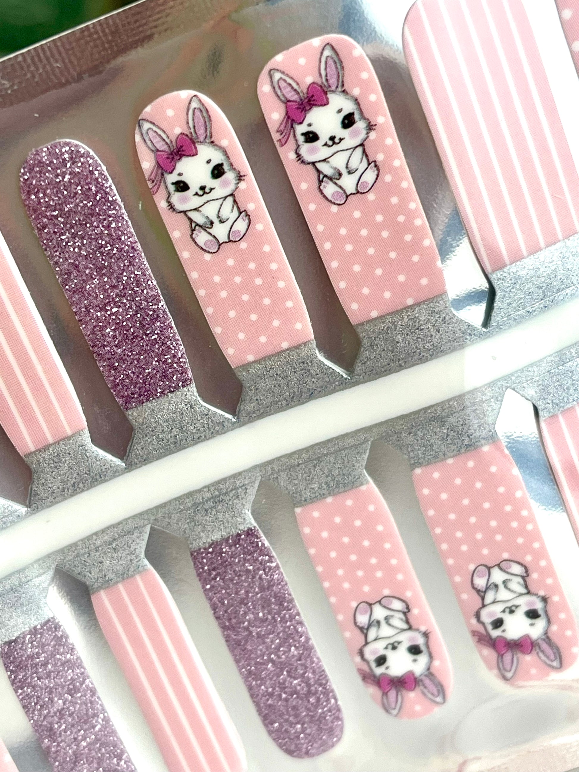 Set of pink and purple glitter nail strips featuring cute white bunnies with pink bows, polka dots, and vertical stripes.